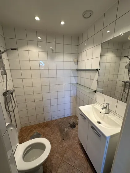 Eldre bad med hvite veggfliser, dusj, servant og toalett
