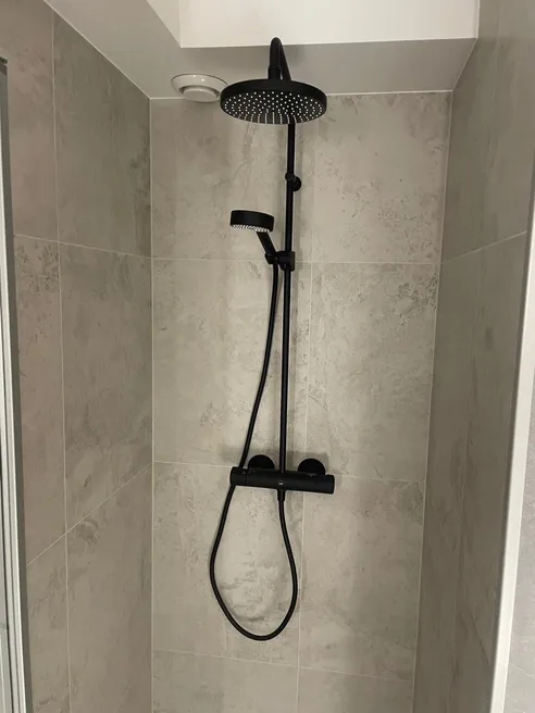 Sort dusjsett med rund takdusj og termostatbatteri på vegg med grå fliser