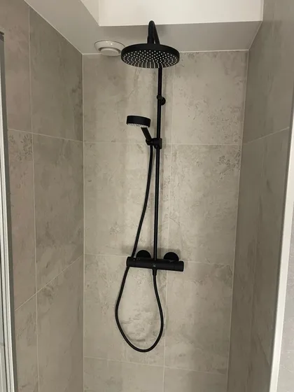 Sort dusjsett med rund takdusj og termostatbatteri på vegg med grå fliser