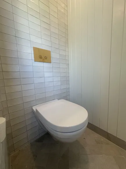 Vegghengt toalett med trykkplate i messing på vegg med lyse fliser