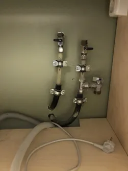 To stengekraner med slanger på veggen i et skap, med avløpsslange og støpsel under